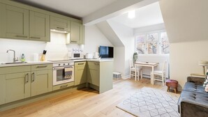 A modern kitchen with green cabinets, a microwave, and a stove. There is a dining area with a table and chairs, and a window with a view of trees. - Bright and modern East London loft (London)