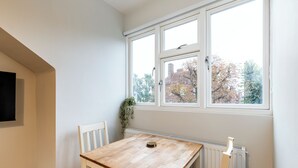 A room with a wooden table and two chairs, a radiator, and a window with a view of trees and buildings. - Bright and modern East London loft (London)