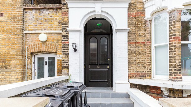 A black door with a green light above it, a white-framed window to the right, and a brick wall with a white door to the left. - Bright and modern East London loft (London)