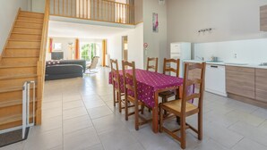 Un amplio salón con mesa de comedor, sillas de madera, una escalera y una zona de cocina.