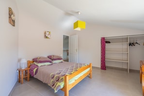 A bedroom with a bed, bedside table, lamp, wardrobe, and a door leading to another room.