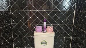Des toilettes avec un abattant et un couvercle blancs, un accessoire de bidet vert et deux objets décoratifs posés sur le couvercle.