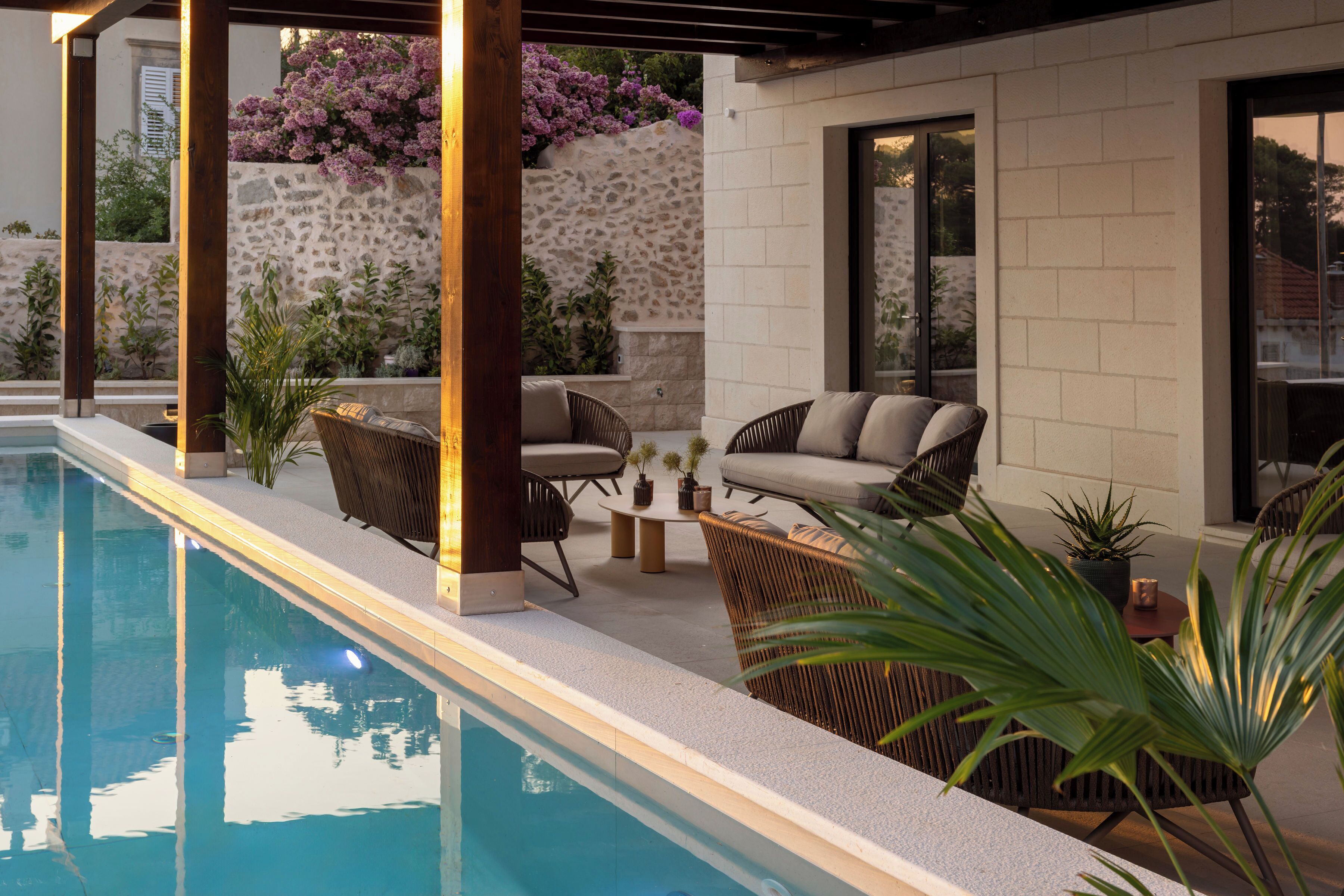 A poolside area with a stone wall, wicker furniture, and potted plants.