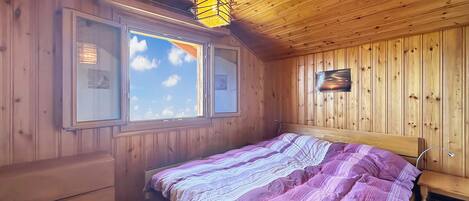 A wooden-paneled room with a bed, a window, and a wall-mounted picture.