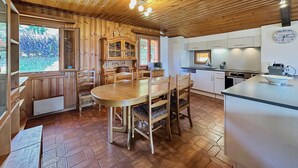 Un intérieur en bois comprenant une table à manger, des chaises, un coin cuisine et une horloge au mur.