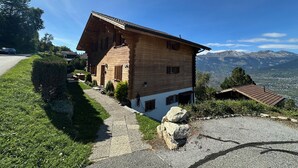 Une maison en bois avec un toit en pente, un chemin de pierres et une vue sur les montagnes en arrière-plan.