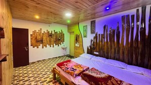 Habitación con techo de madera, cama con ropa de cama floral, una obra de arte de madera en la pared y un suelo con patrón de espiga.