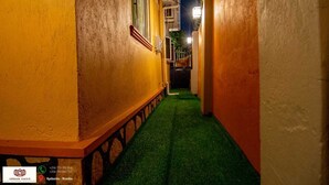 Une ruelle étroite avec un chemin bordé d’herbe artificielle verte, flanquée d’immeubles aux murs jaunes et blancs.