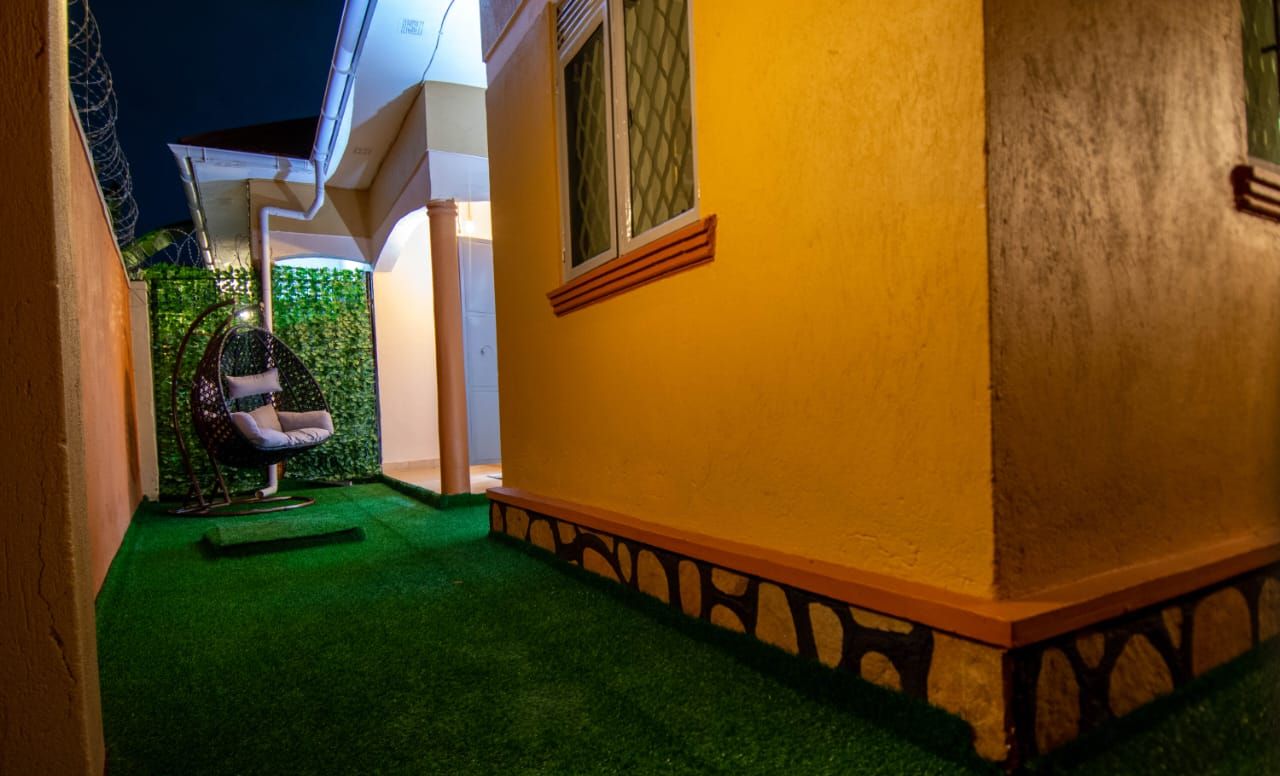 Un sendero estrecho que conduce a un edificio con fachada amarilla y una ventana con persiana de diseño geométrico.