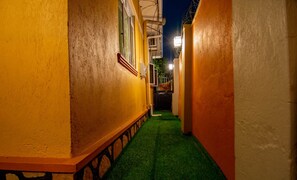 Un estrecho callejón con un sendero de césped artificial verde, bordeado por edificios de paredes amarillas y blancas.