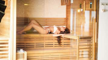 A person lying on a wooden bench inside a sauna room with a brick wall and wooden slats.