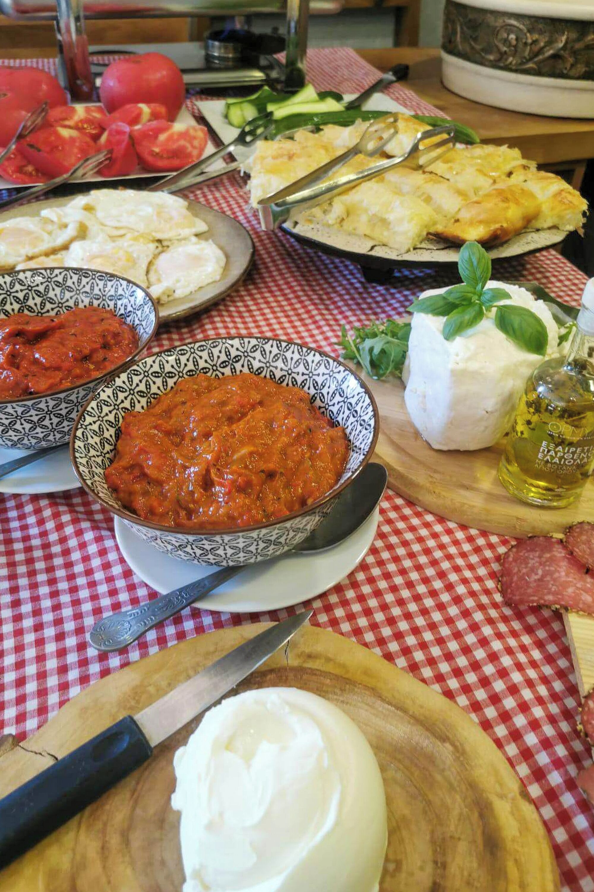 Une table sur laquelle on trouve divers plats, notamment un bol de sauce tomate, une assiette de tomates en tranches, un bol de fromage et une planche à découper en bois avec un couteau.