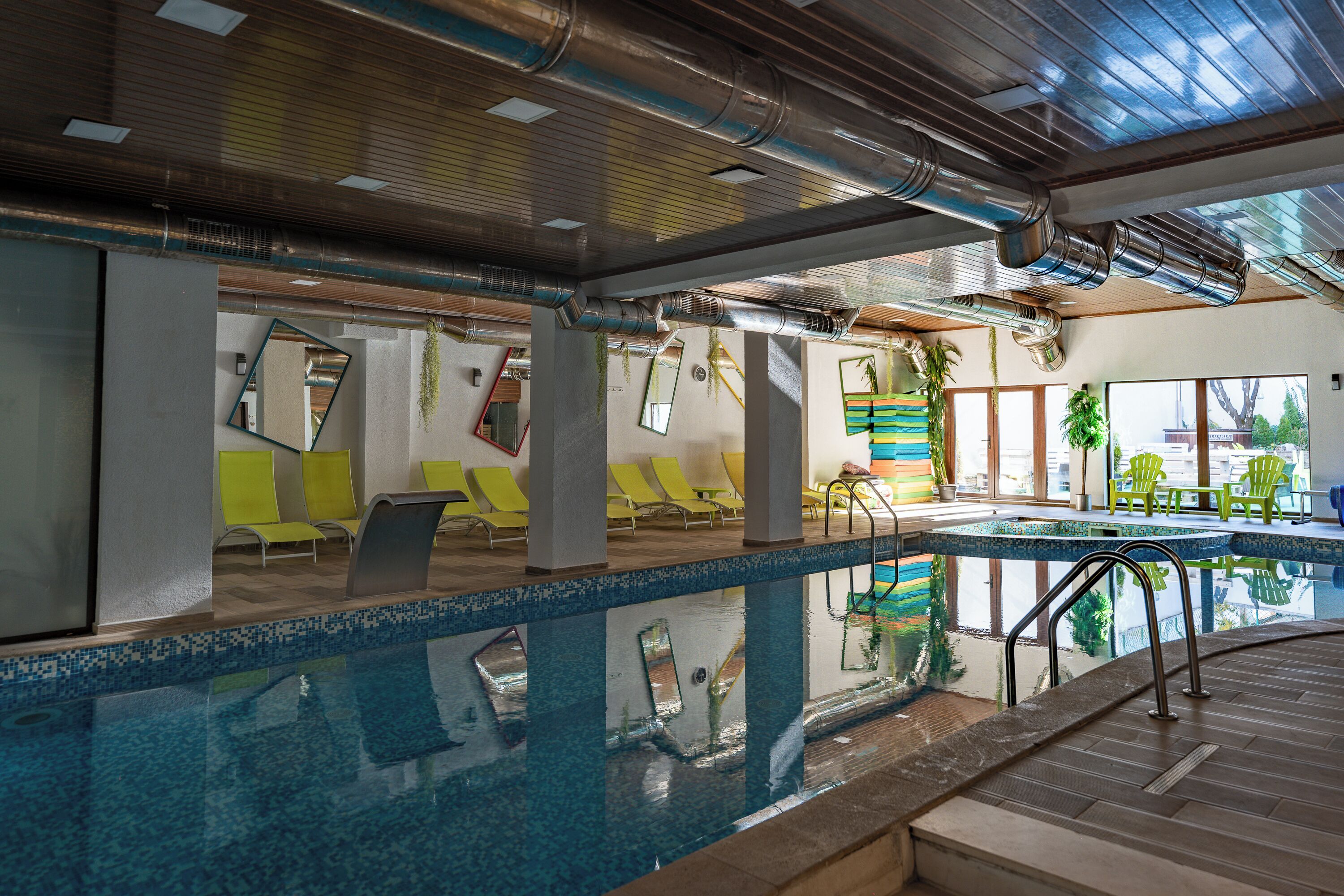 Una piscina interior con agua cristalina, rodeada de sillas amarillas y un tragaluz.