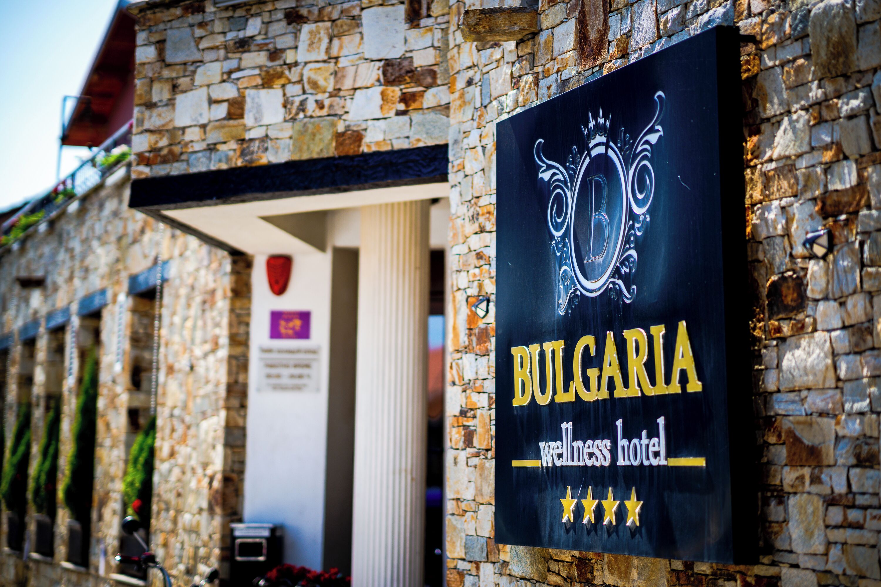A sign for Bulgaria Wellness Hotel, featuring a stone facade and a black signboard with a crown emblem.