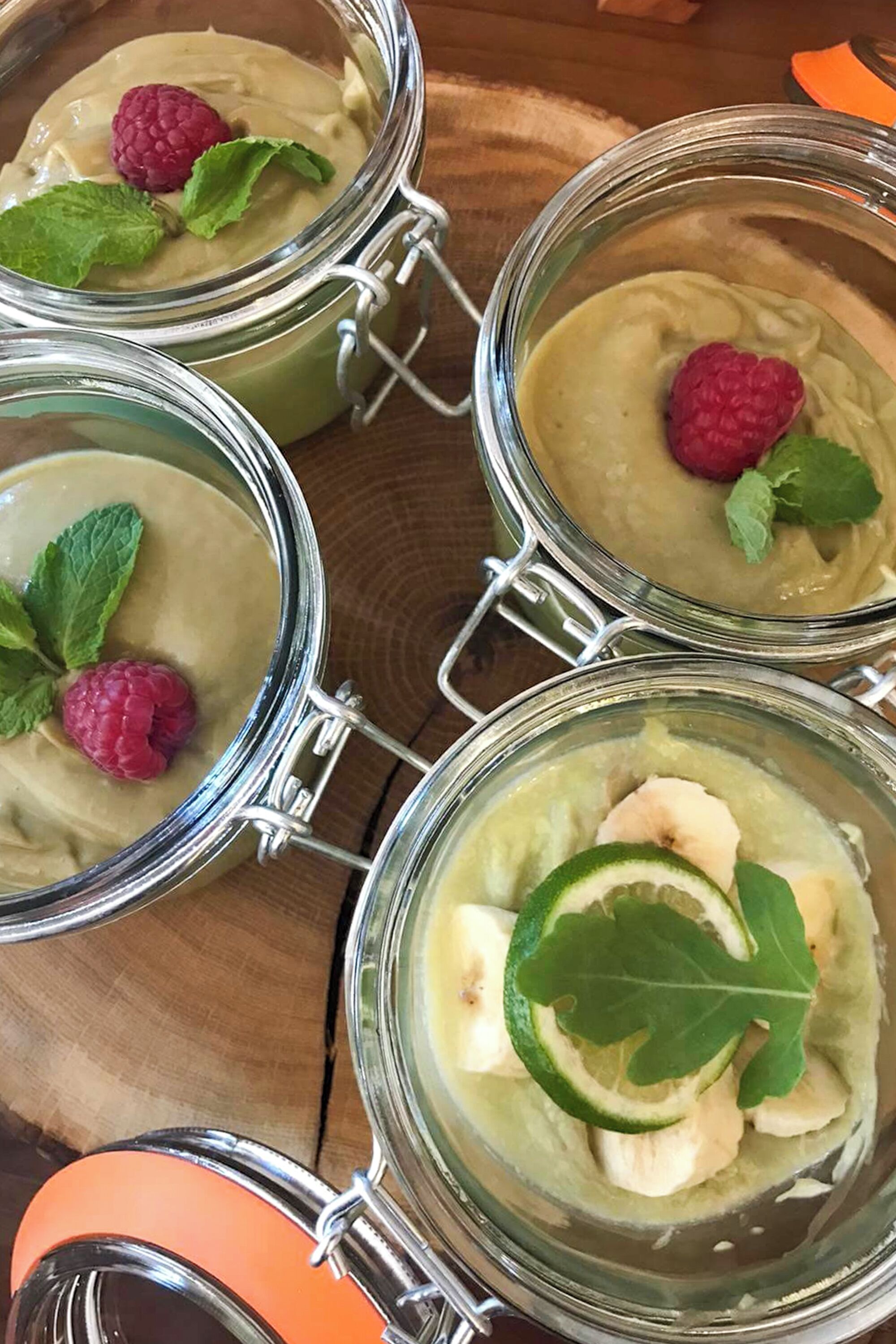 Four glass jars with metal clasps, each containing a creamy substance, garnished with a raspberry and mint leaves.