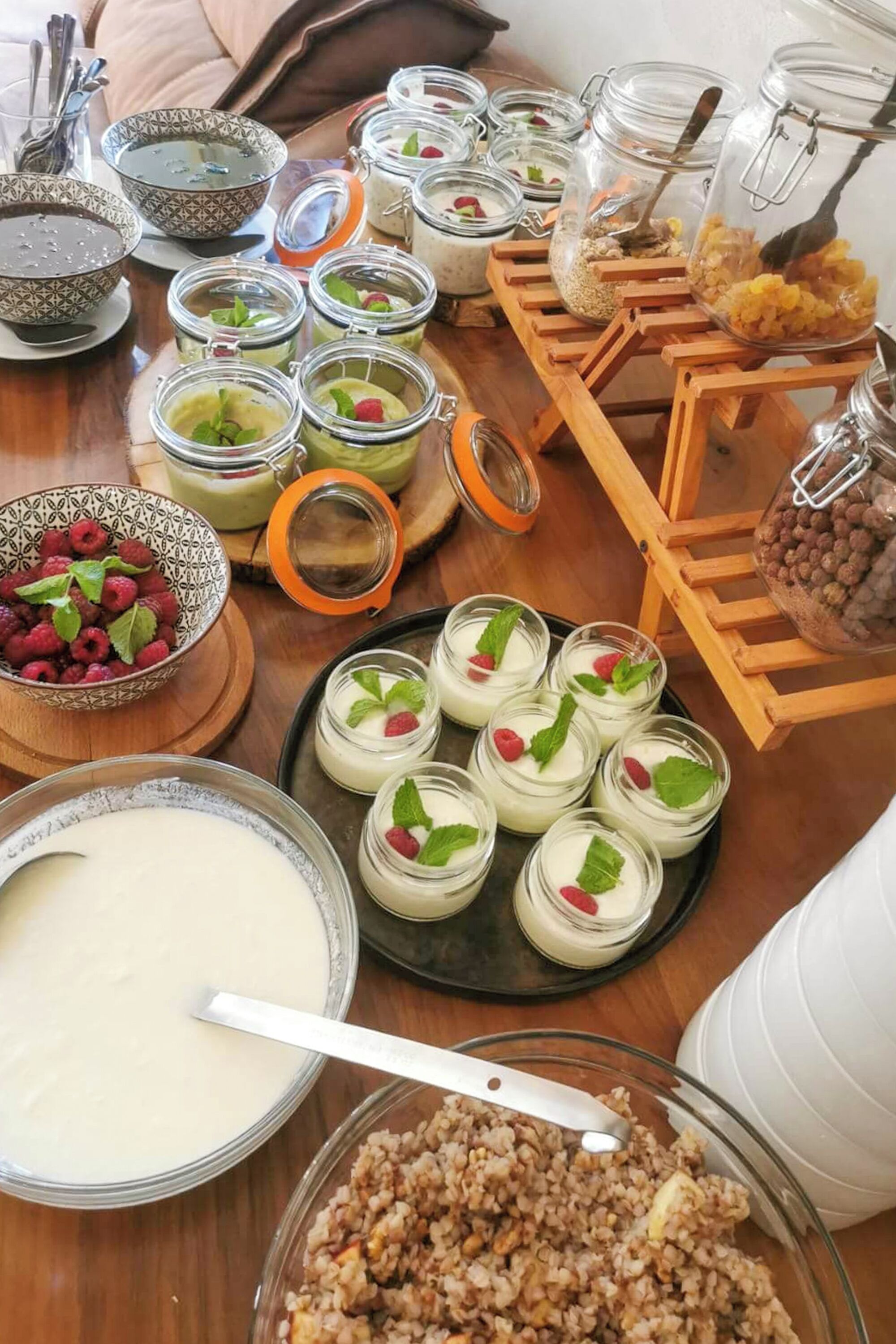 A table with various food items including bowls of soup, jars of yogurt with raspberries, and bowls of granola.