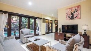 A spacious living area with a sofa, chairs, a coffee table, a TV, and a painting on the wall. - 2BR Private Pool Tiga Samudra Villa (badung)