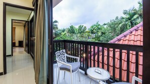 A balcony with a white chair, a small table, and a view of a red-roofed building and lush greenery. - 2BR Private Pool Tiga Samudra Villa (badung)