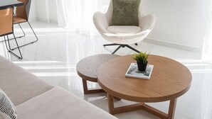 Un soggiorno moderno con un tavolino rotondo in legno, una poltrona bianca con cuscino verde e un divano beige.