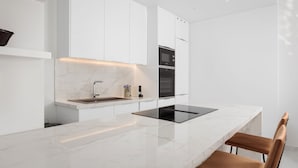 Una cucina moderna con mobili bianchi, un piano di lavoro in marmo e un piano cottura a induzione nero.
