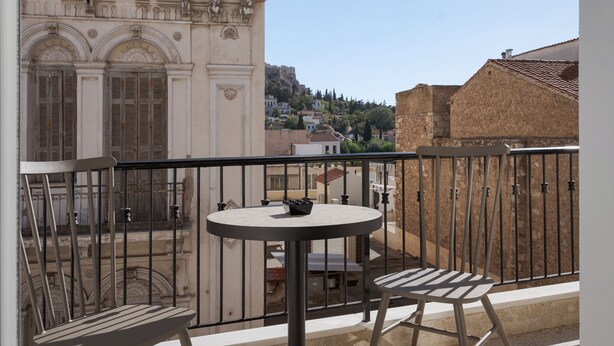 Un balcone con un tavolino rotondo e due sedie, affacciato su un edificio storico con finestre ad arco e un muro in pietra.