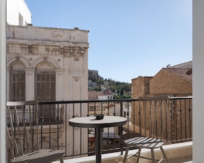 A balcony with a round table and two chairs, overlooking a historic building with arched windows and a stone wall. - Athenian Acropolis Residence (Athens)