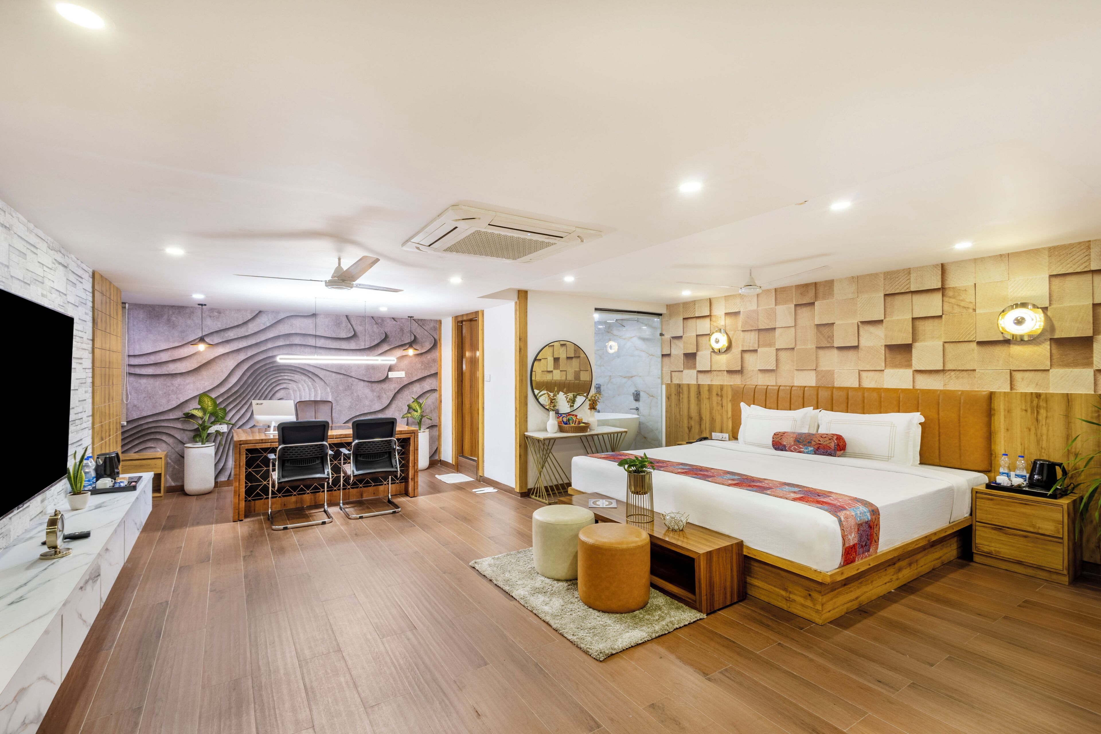 Une chambre d’hôtel moderne avec un plancher en bois, un grand lit, un bureau avec deux chaises, une coiffeuse avec un miroir et un téléviseur.