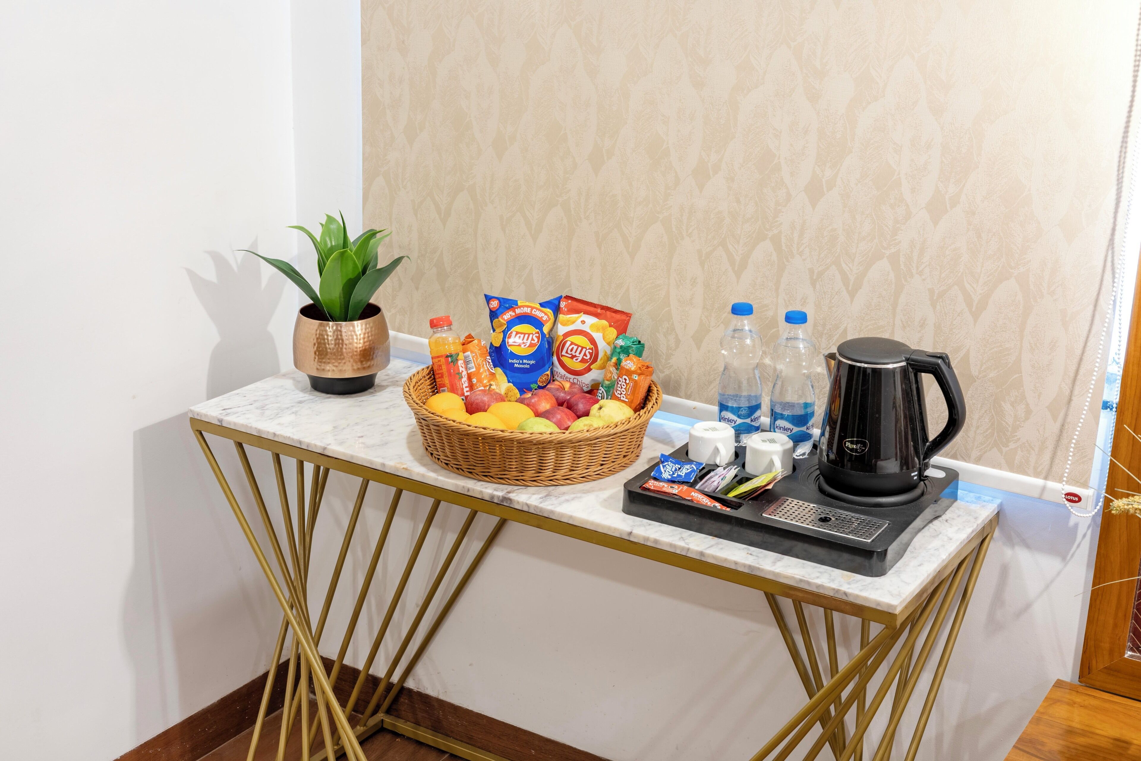 A marble countertop with a basket of fruits, snacks, a kettle, and bottled water.