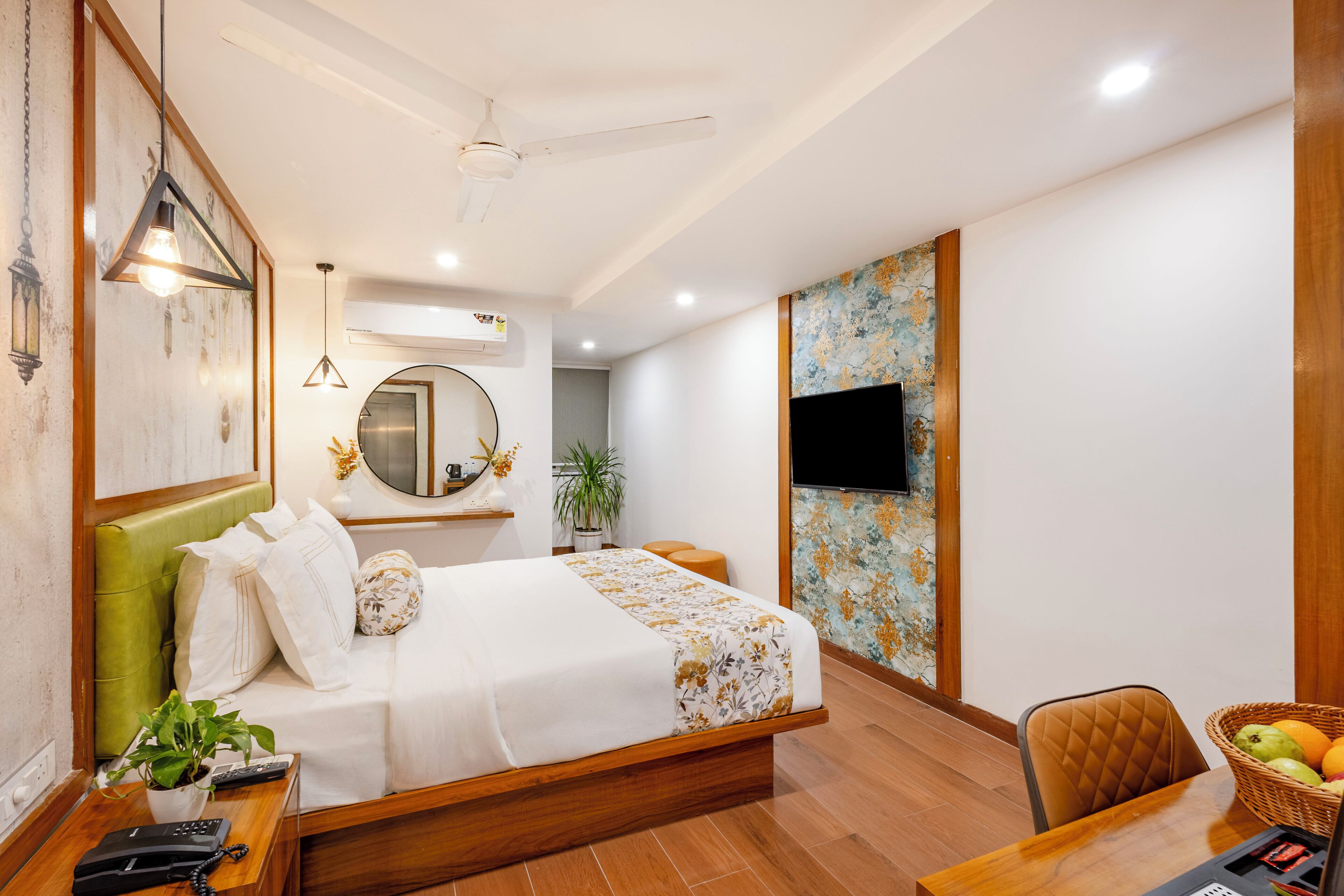 A hotel room with a bed, a desk with a chair, a television, and a wall with a decorative pattern.