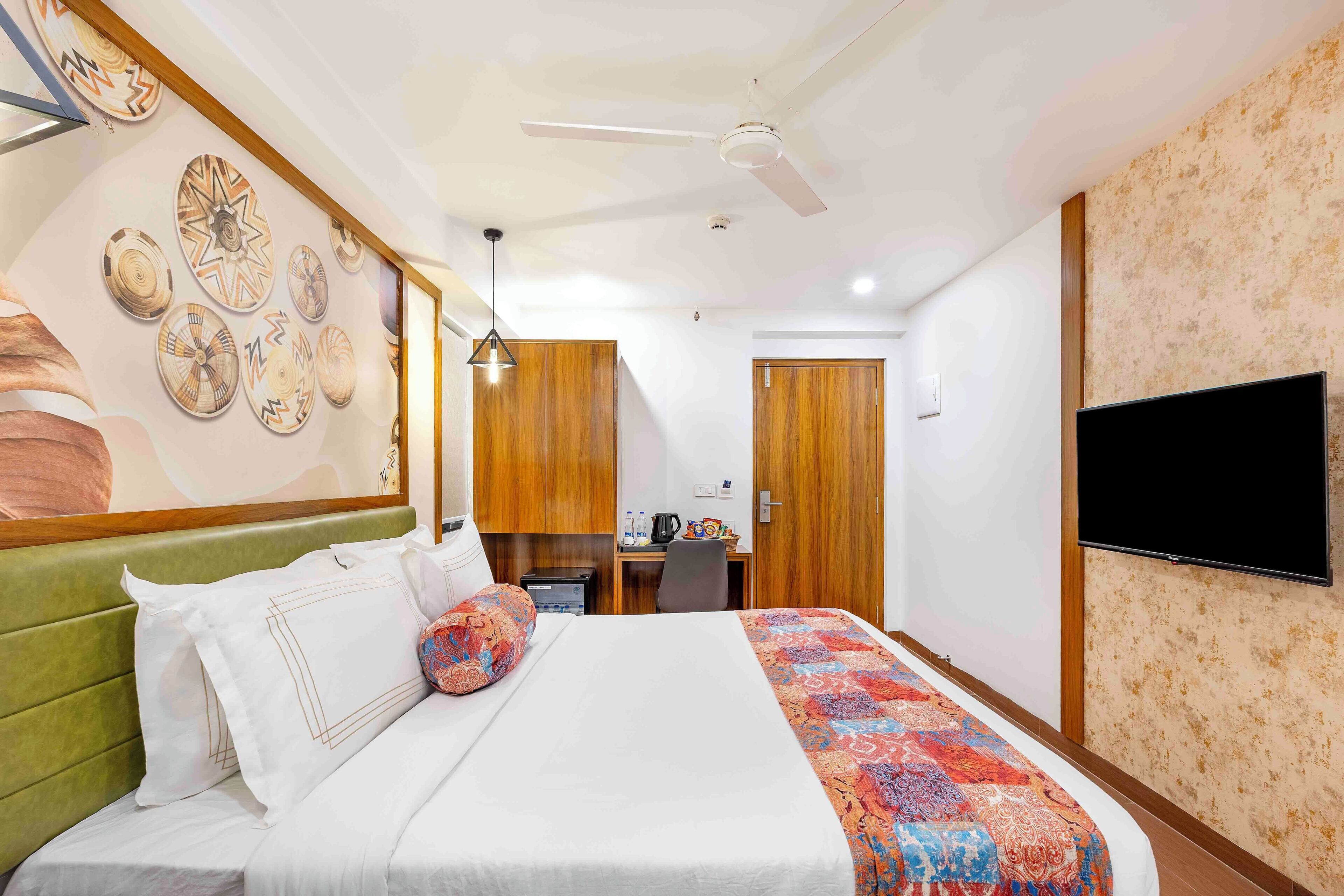 A hotel room with a bed, a desk, a chair, a television, and a ceiling fan.
