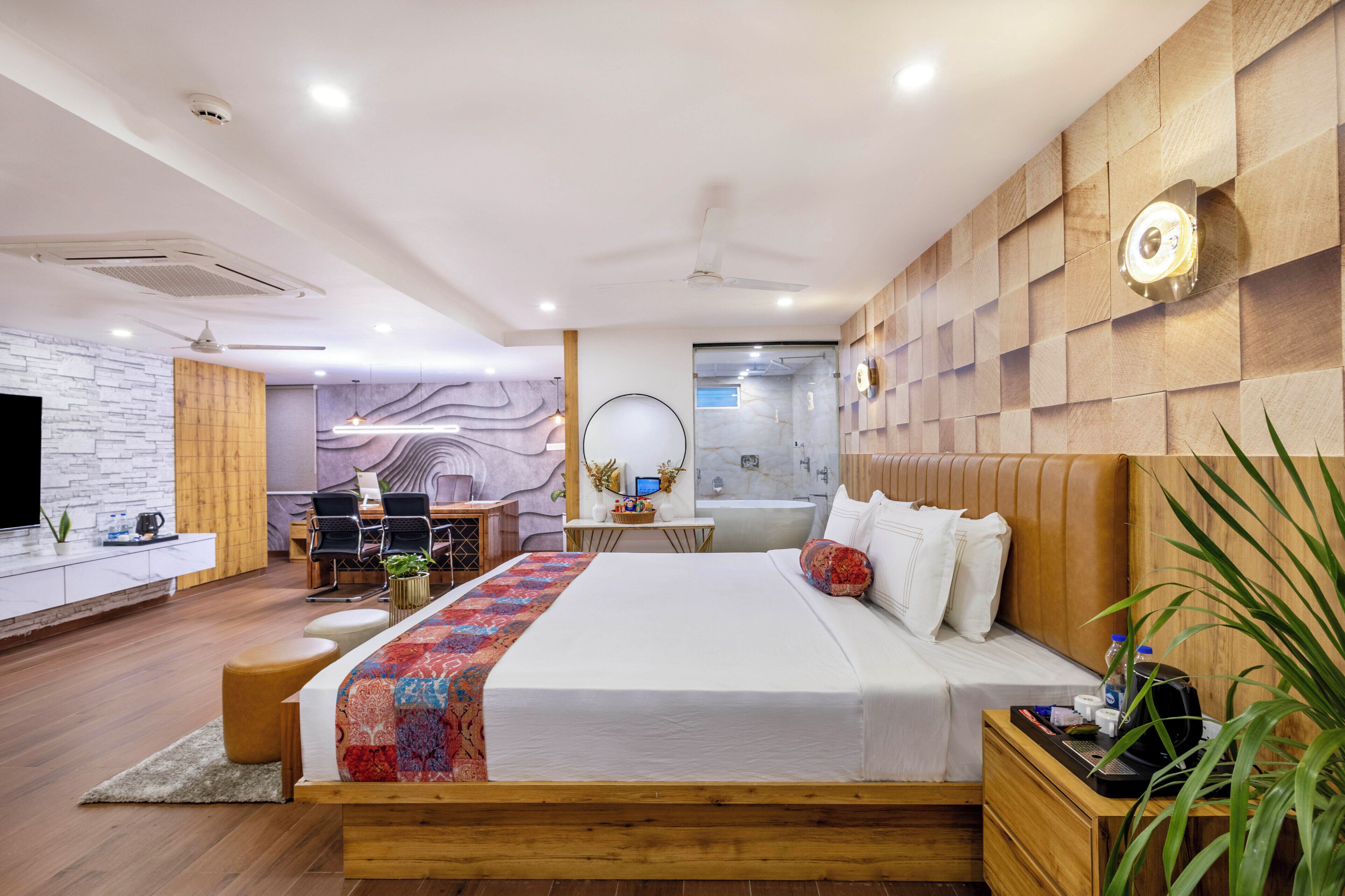 Una habitación de hotel moderna con cabecera de madera, una cama grande, un escritorio con silla, un baño pequeño y una zona de estar con sofá y mesa de centro.