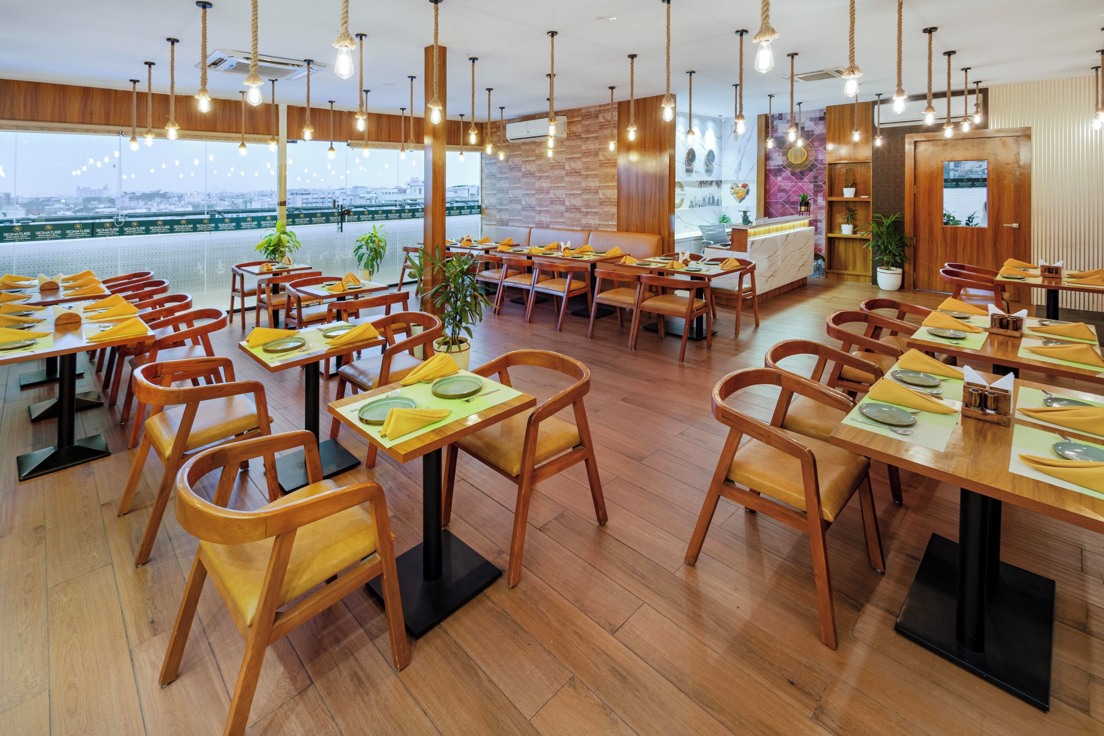 Un restaurante con mesas y sillas de madera, vistas a la ciudad y lámparas colgantes.
