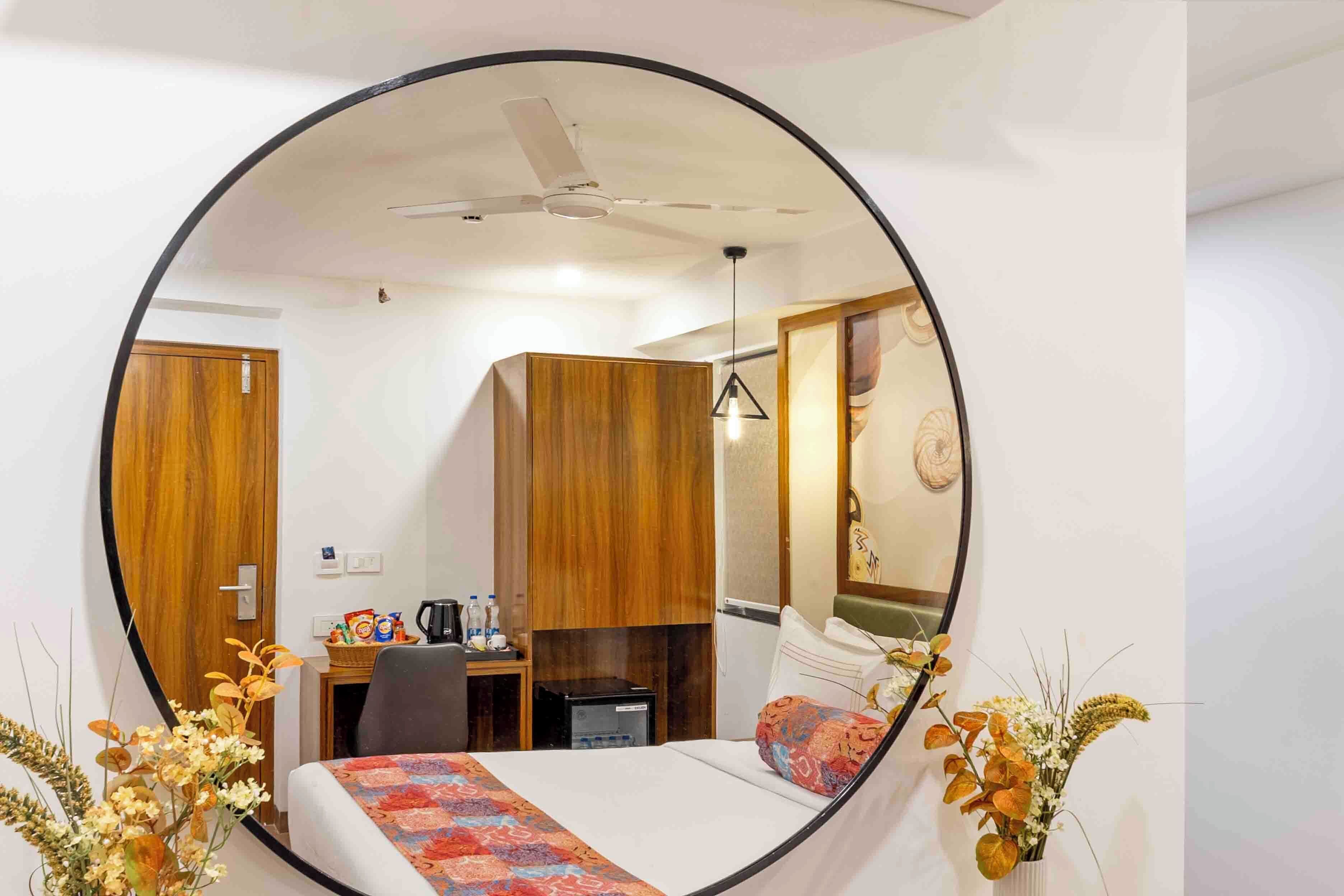 A hotel room with a bed, a desk, a chair, a mirror, a ceiling fan, and a wall-mounted clock.