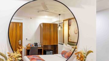 A hotel room with a bed, a desk, a chair, a mirror, a ceiling fan, and a wall-mounted clock.
