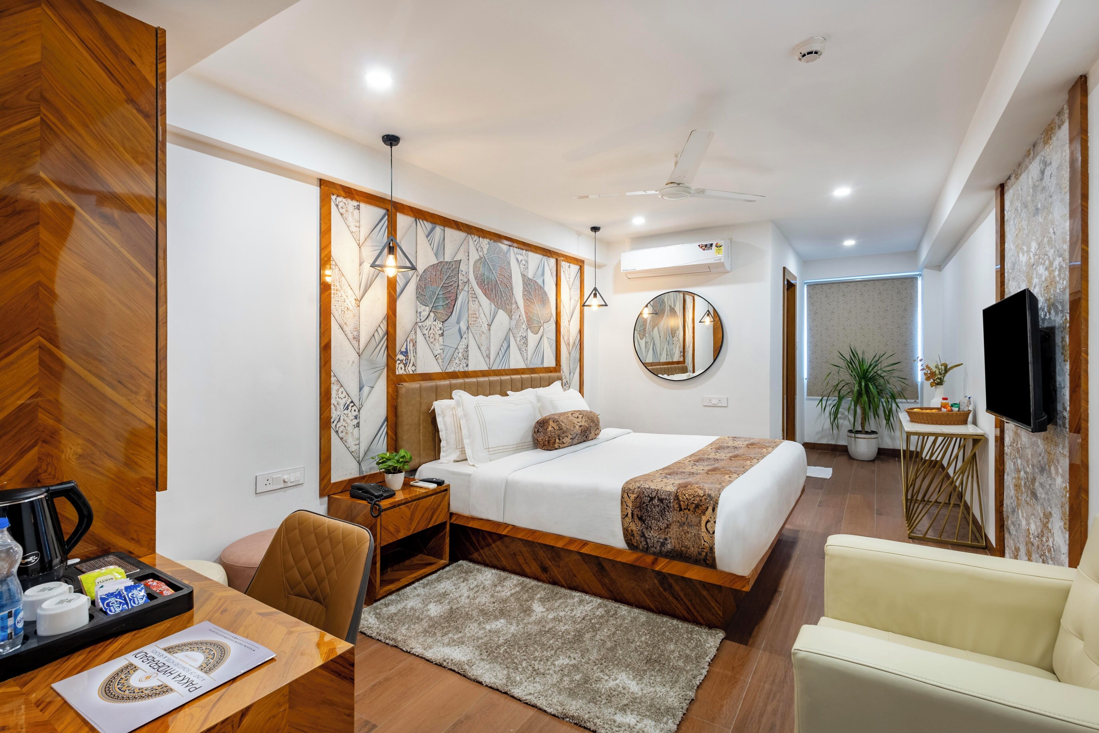A modern hotel room with a bed, a desk, a chair, a television, and a potted plant.