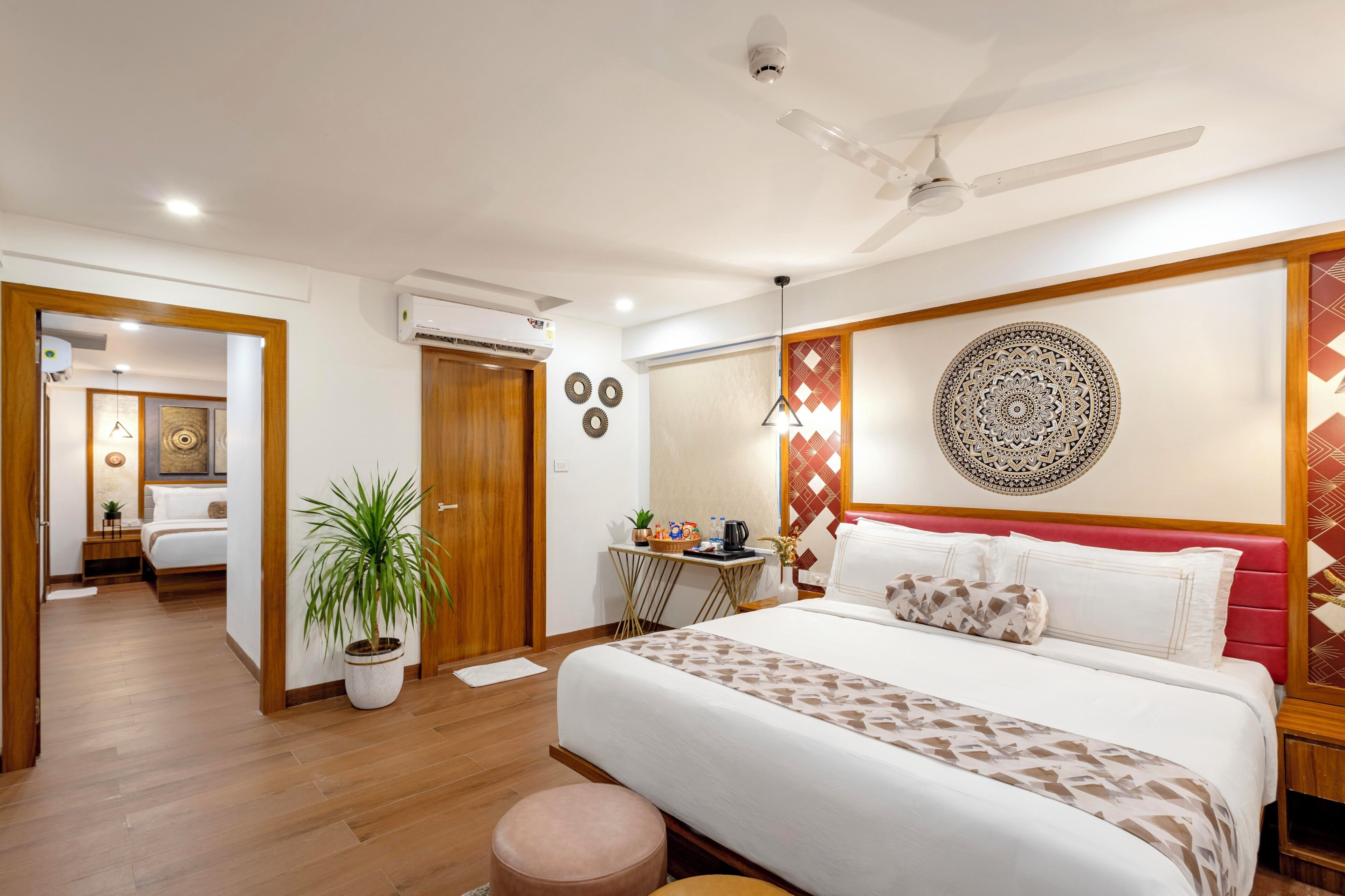 A hotel room with a bed, a desk, a potted plant, a ceiling fan, and a wall with decorative patterns.