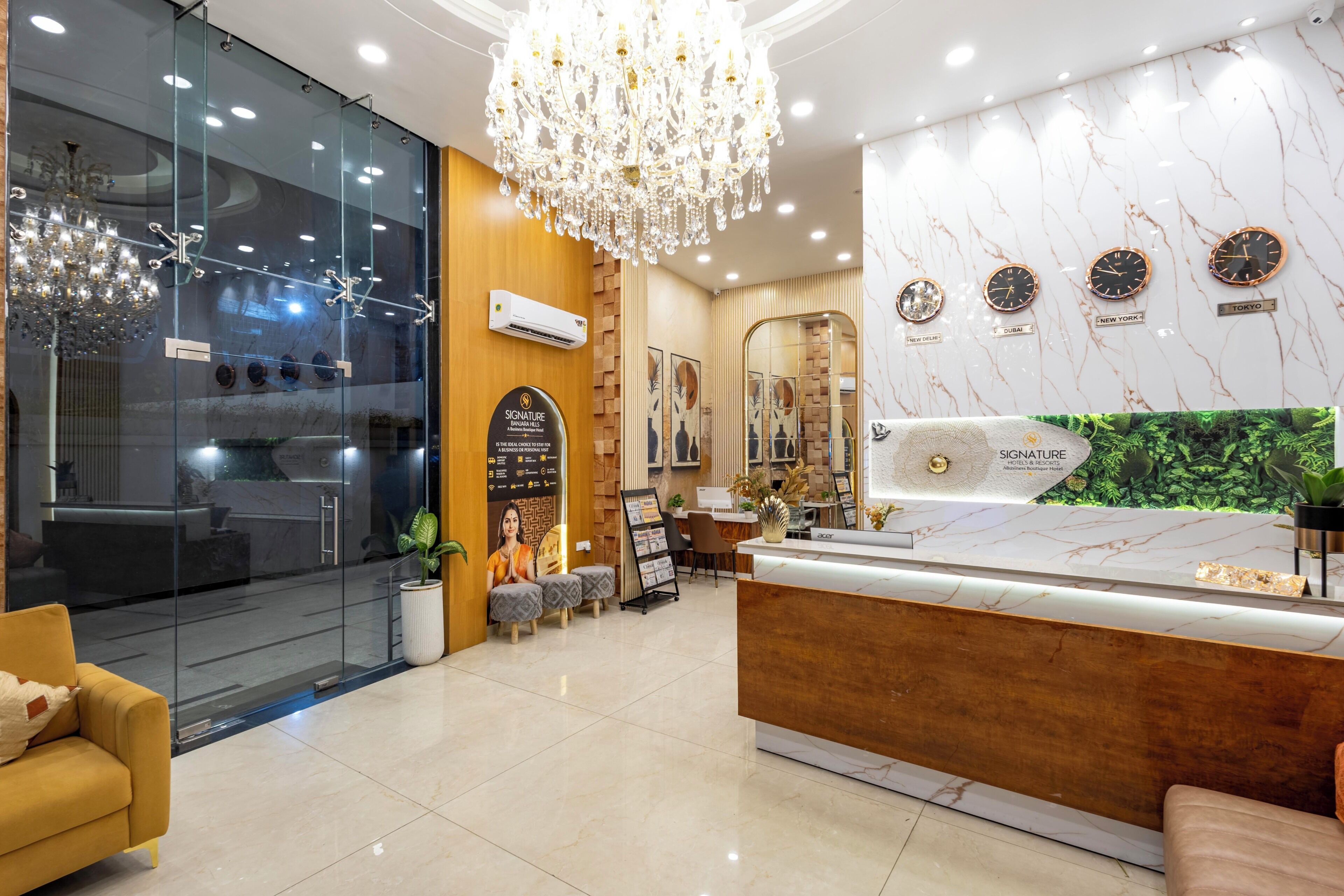 A hotel reception area with a marble wall, a chandelier, a reception desk, and a seating area with a plant.