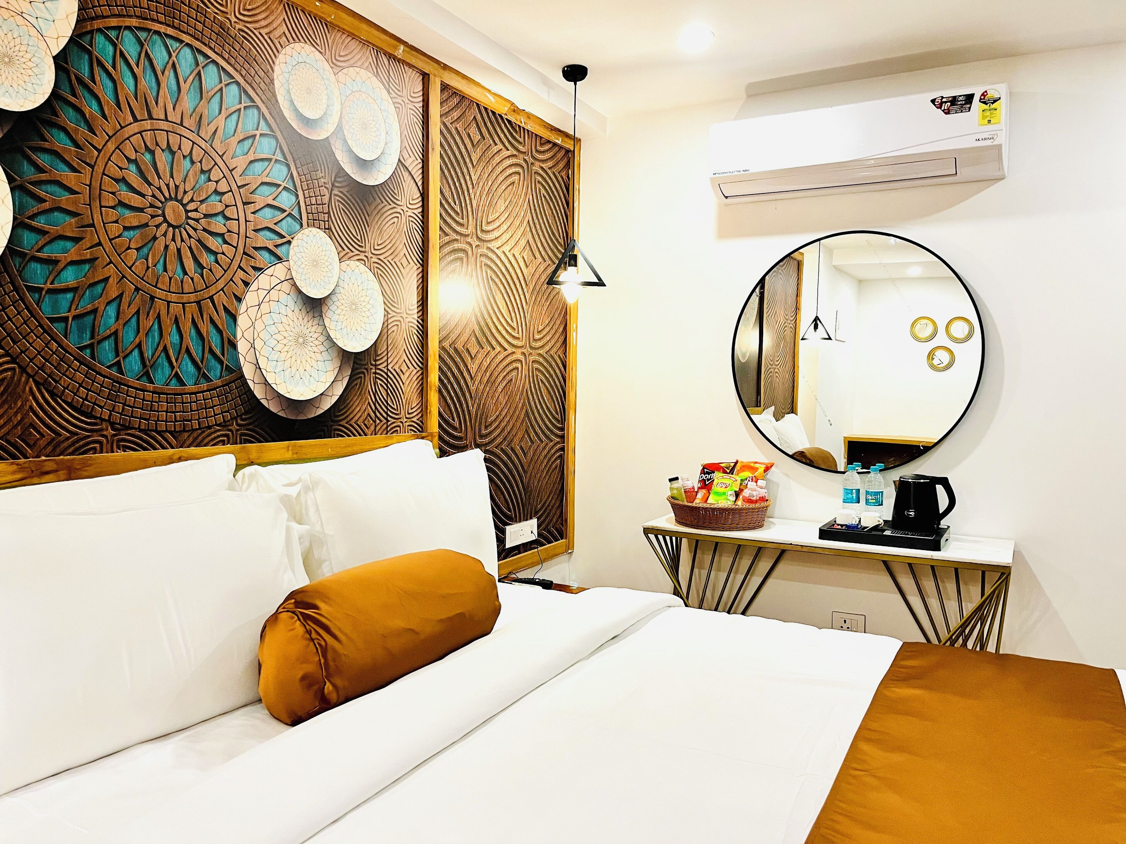 A hotel room with a bed, a bedside table with a basket of snacks, a round mirror, and a wall with intricate wood paneling.