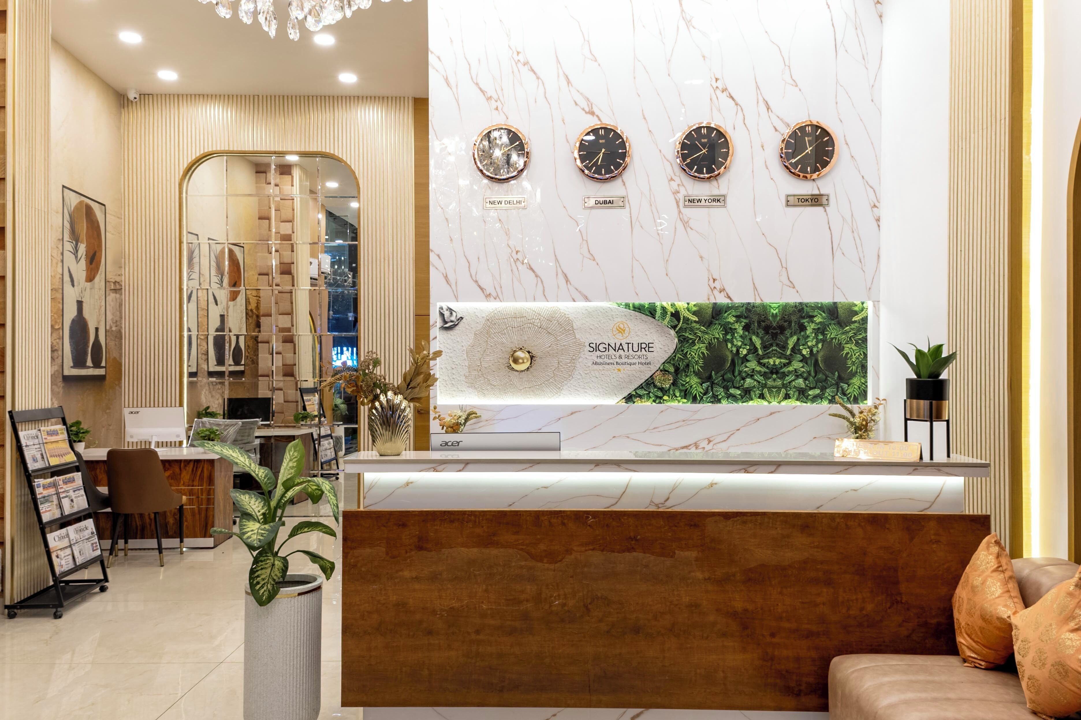 A hotel reception desk with a marble wall, clocks indicating different cities, and a plant display.