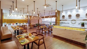 Un restaurante con mesas y sillas de madera, lámparas colgantes y un mostrador de recepción de mármol.