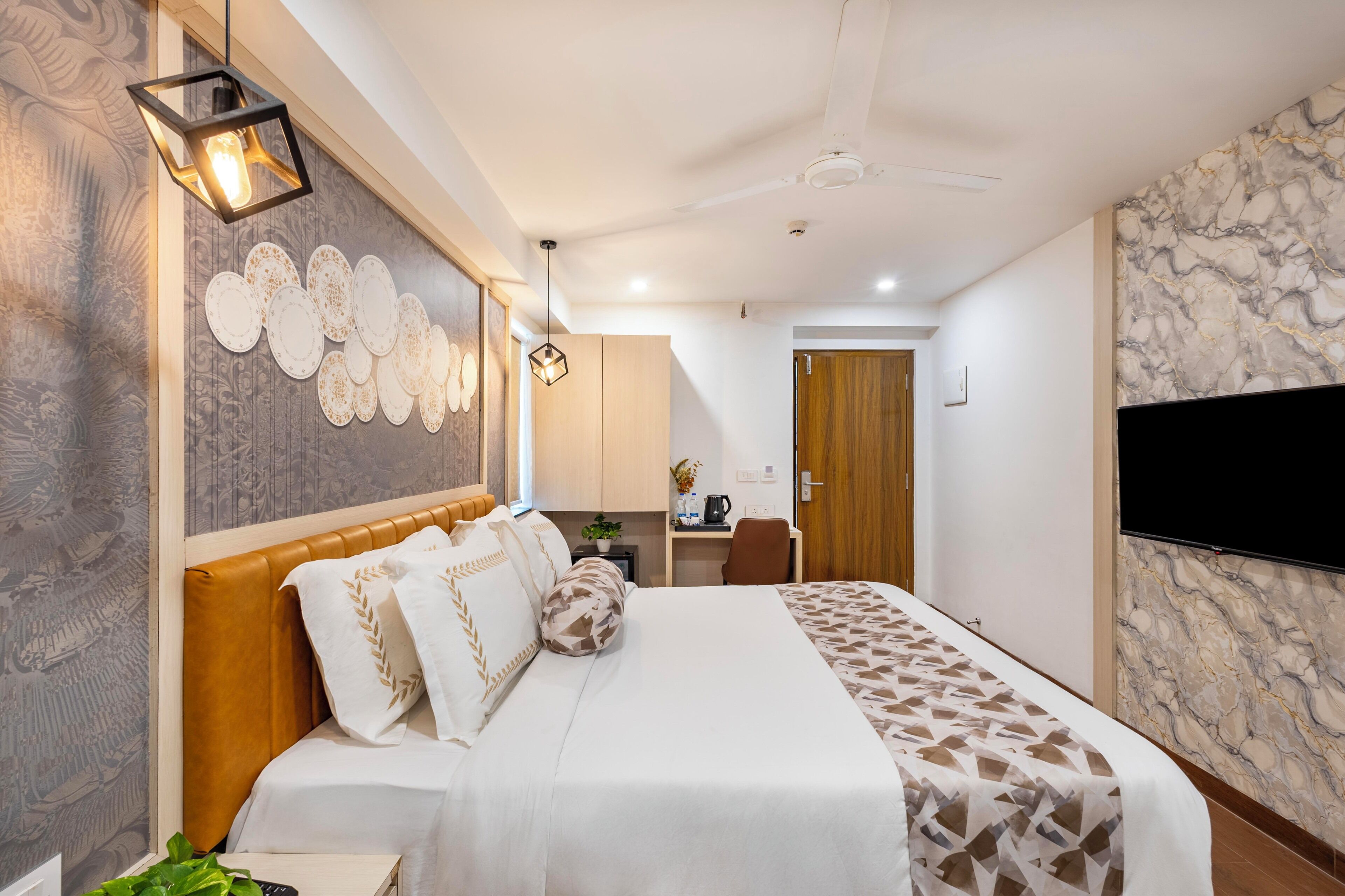 A modern bedroom with a bed, a desk, a chair, a TV, and a ceiling fan.