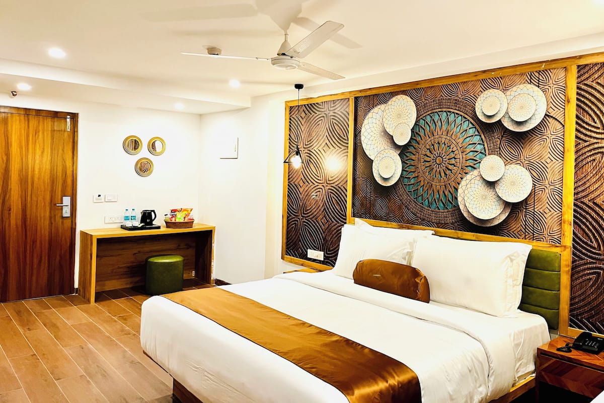 A hotel room with a large bed, a desk with a chair, a ceiling fan, and decorative wall panels.