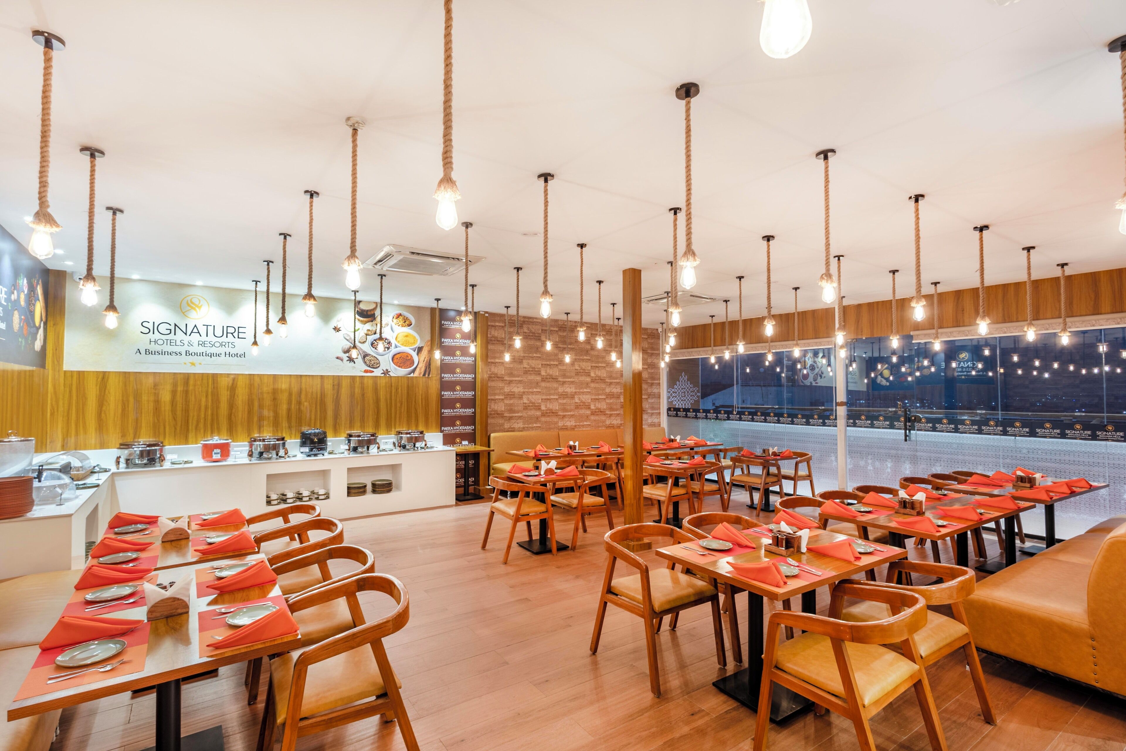 Un restaurante con mesas y sillas de madera, lámparas colgantes y vistas a la ciudad.