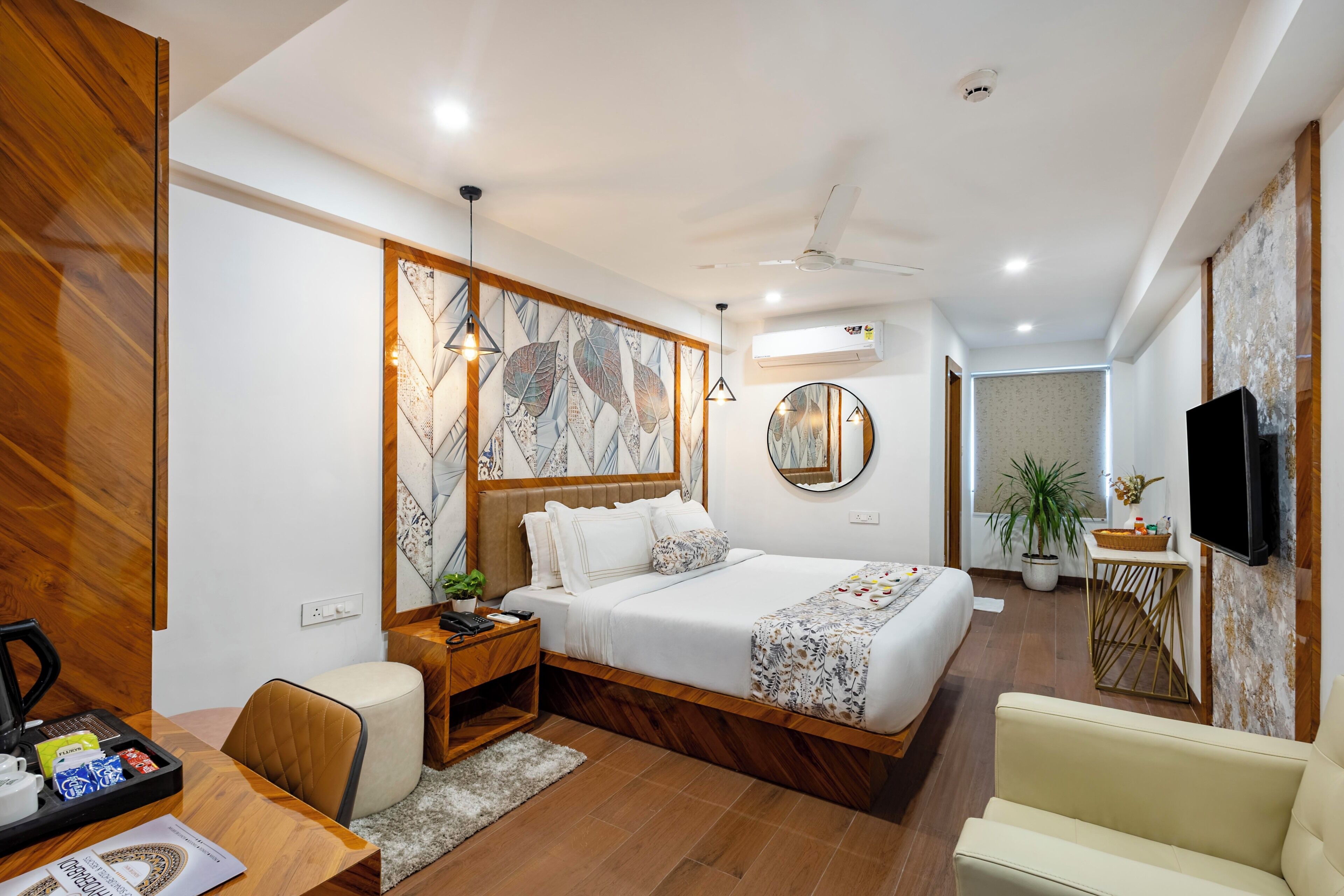 A modern hotel room with a bed, a desk with a chair, a TV, and a potted plant.