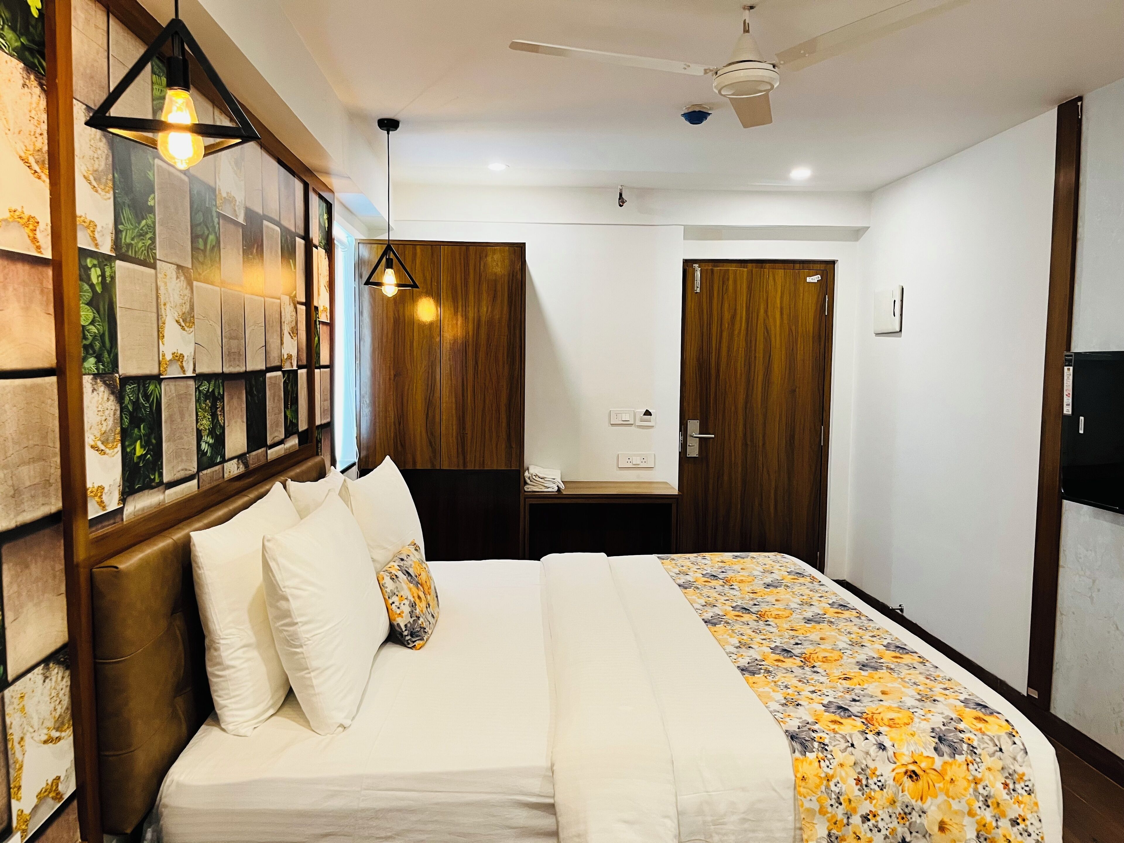 A neatly arranged hotel room with a bed, a wooden headboard, a desk, and a wardrobe.