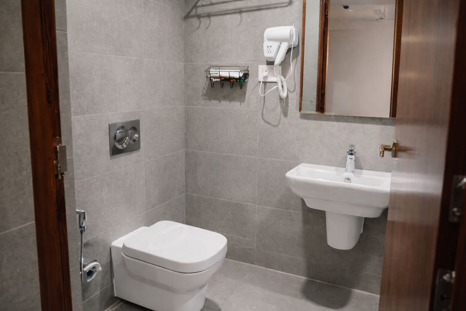 Un baño pequeño y moderno con inodoro, lavamanos y secador de pelo en un soporte de pared.