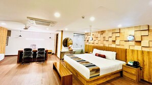 Una habitación de hotel moderna con cabecera de madera, una cama grande, una mesita de noche con lámpara, un banco y un escritorio con silla.