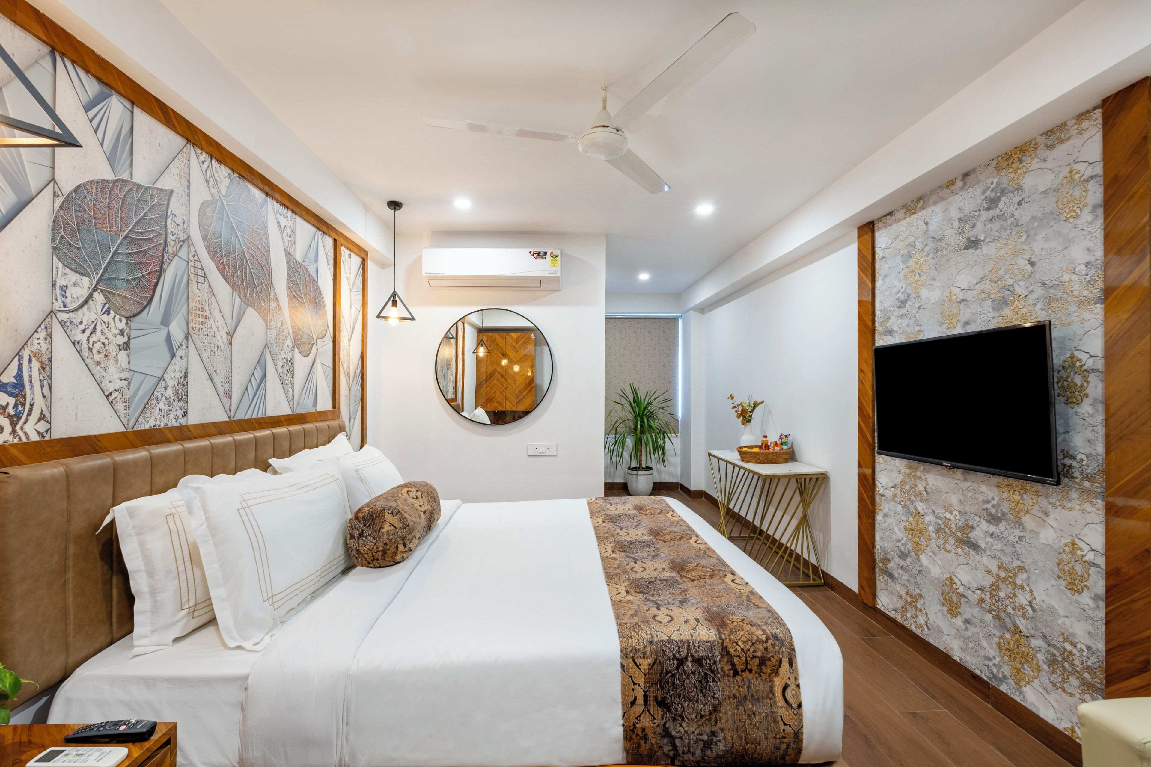 A modern hotel room with a large bed, a flat-screen TV, a ceiling fan, and a decorative wall with leaf patterns.