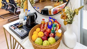 Zona de recepción de un hotel con una estación de café, una cesta de frutas y un espejo que refleja la habitación.