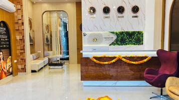 A modern hotel lobby with a reception desk, a chandelier, a sofa, and a decorative flower arrangement on the floor.